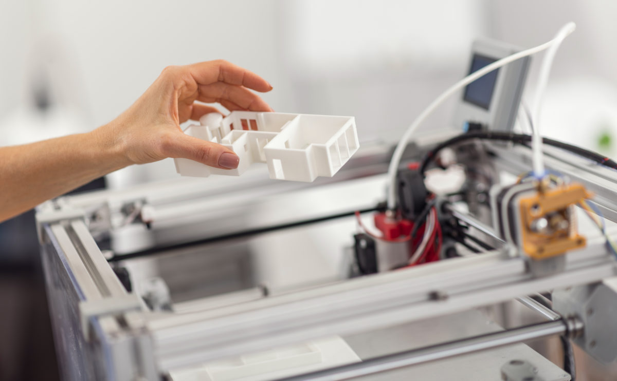 Female hand removing house model from 3D printer