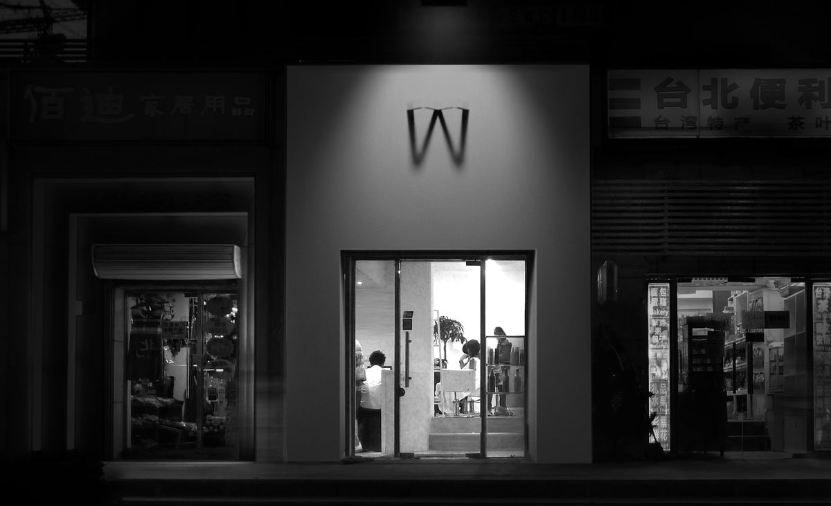 AQSO arquitectos office. La fachada exterior del salón de peluquería tiene un cartel luminoso que proyecta la sombra de la letra W sobre una pared blanca. Es un cartel y un logo original.