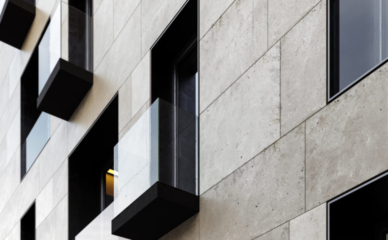 AQSO arquitectos office. Detalle de uno de los balcones. Un simple forjado cubierto con un forro de metal oscuro sobresale del plano de fachada y se cierra con una barandilla de cristal sin marco, contrastando con el aplacado de piedra arenisca.