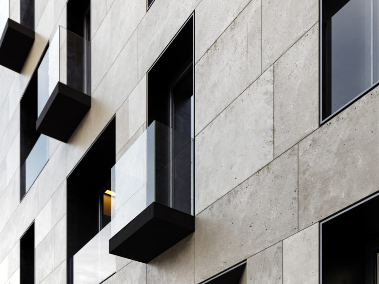 AQSO arquitectos office. Detalle de uno de los balcones. Un simple forjado cubierto con un forro de metal oscuro sobresale del plano de fachada y se cierra con una barandilla de cristal sin marco, contrastando con el aplacado de piedra arenisca.