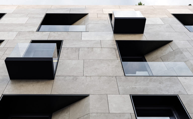 AQSO arquitectos office. La sobria fachada combina tres materiales: piedra arenisca, metal oscuro y vidrio. La disposición de los huecos ofrece un aspecto dinámico basado en simples desplazamientos, esquinas achaflanadas y alineación de huecos.