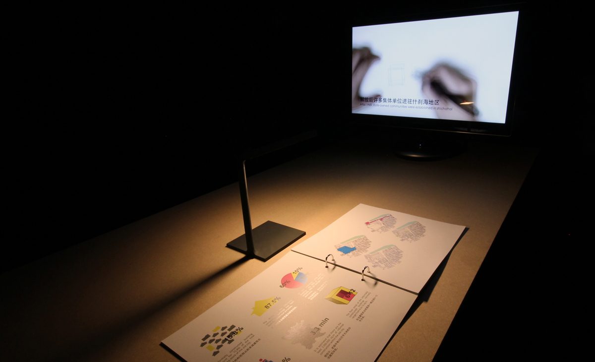 AQSO arquitectos office. Cada proyecto de la exposición se muestra en una mesa que tiene un libro con contenido gráfico y una pantalla con un vídeo documental.