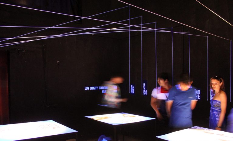 AQSO arquitectos office. La sala de exposiciones princial es un espacio oscuro con cuatro mesas iluminadas que corresponden a los principios de la investigación urbana.