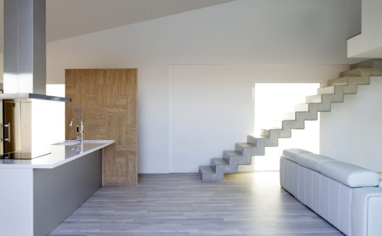 AQSO arquitectos office. El interior de la vivienda combina suelos de madera gris con piedra travertina y el hormigón expuesto de las escaleras.