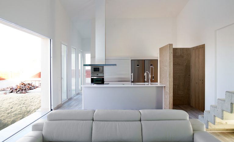 AQSO arquitectos office. Desde el espacio diáfano del salón se ve la cocina con una isla central, un frigorífico doble y un extractor colgado del techo.