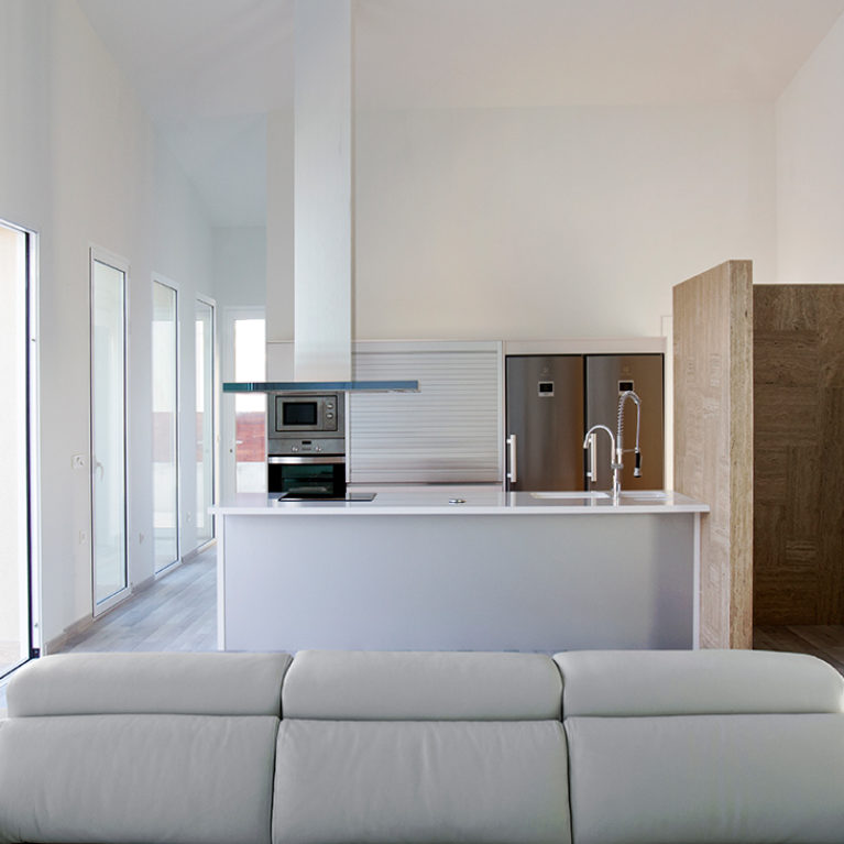 AQSO arquitectos office. Desde el espacio diáfano del salón se ve la cocina con una isla central, un frigorífico doble y un extractor colgado del techo.