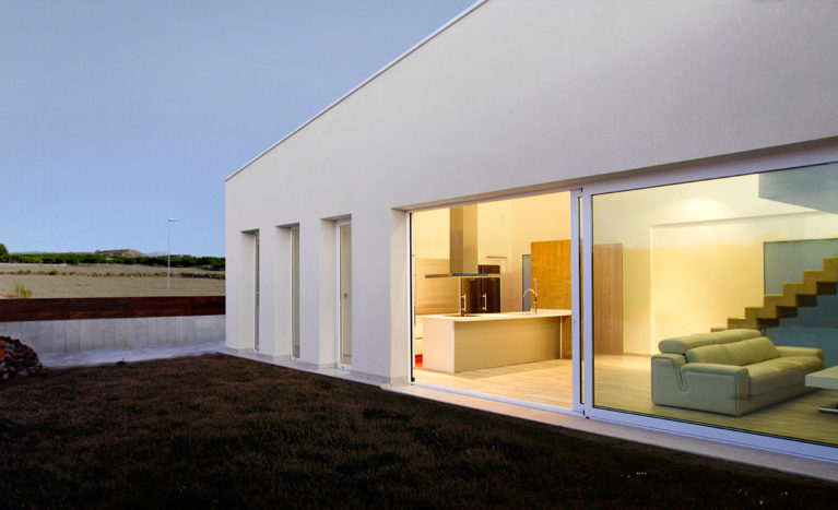 AQSO arquitectos office. In the evening, the large living room window illuminates the front garden, from which you can see the white mountains surrounding the house.