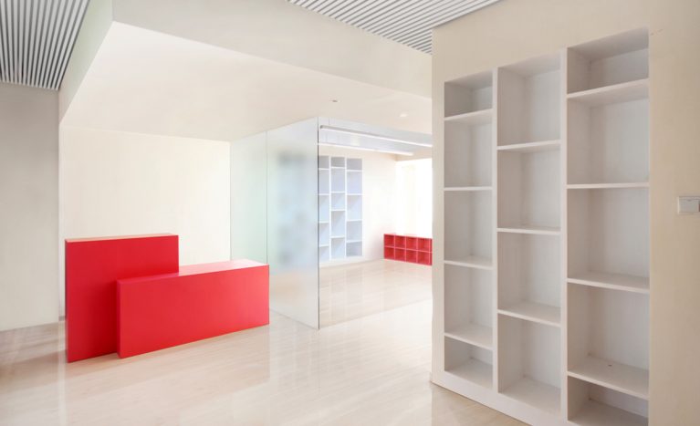 AQSO arquitectos office. La entrada tiene una sala de espera que conecta con la zona de talleres. El diseño interior es luminoso y combina particiones de vidrio translúcido con muebles sencillos de colores.