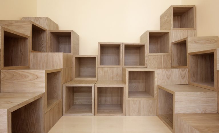AQSO arquitectos office. La biblioteca infantil está formada por una composición de cubos de madera que pueden agruparse para formar un mueble escalable donde guardar libros y sentarse a leer.