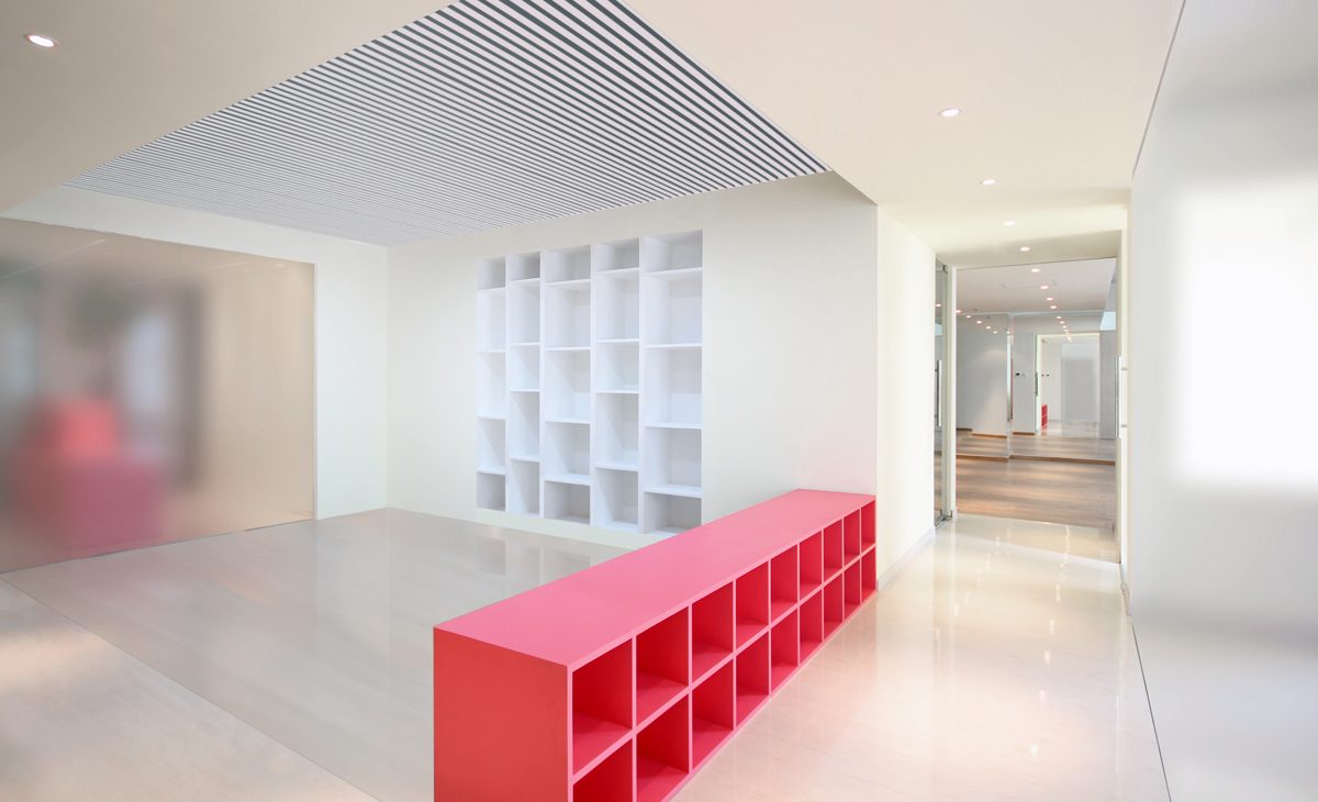 AQSO arquitectos office. En en la parte central del local se sitúa la zona de talleres, que cuenta con un mueble bajo de madera lacada de color rosa y una estantería integrada en la pared.