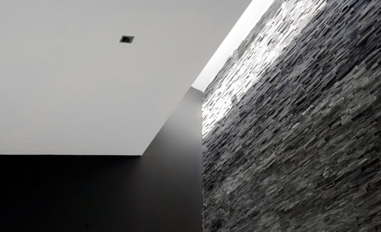 AQSO arquitectos office. El lucernario alargado que abre el techo a lo largo del muro de piedra subraya la textura de la mampostería de pizarra y contrasta con el muro pintado de negro.