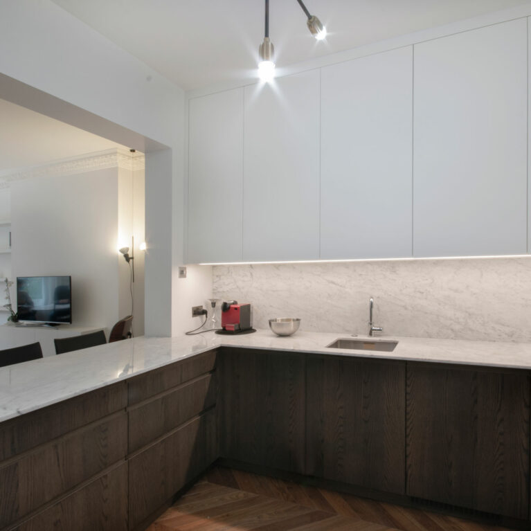 AQSO arquitectos office. The kitchen opens onto the living room thanks to a large opening with structural reinforcement in the load-bearing wall. The kitchen units combine dark wood, marble worktop and matt white lacquered doors.